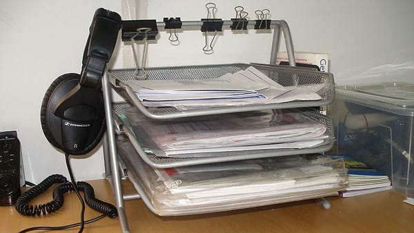 Three stacked inbox trays on an office desk, each filled with papers waiting to be worked through